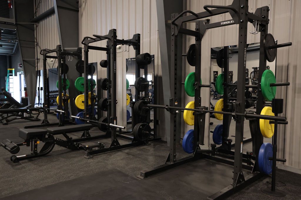 three sets of squat racks with colorful weights and bars for weight liftng
